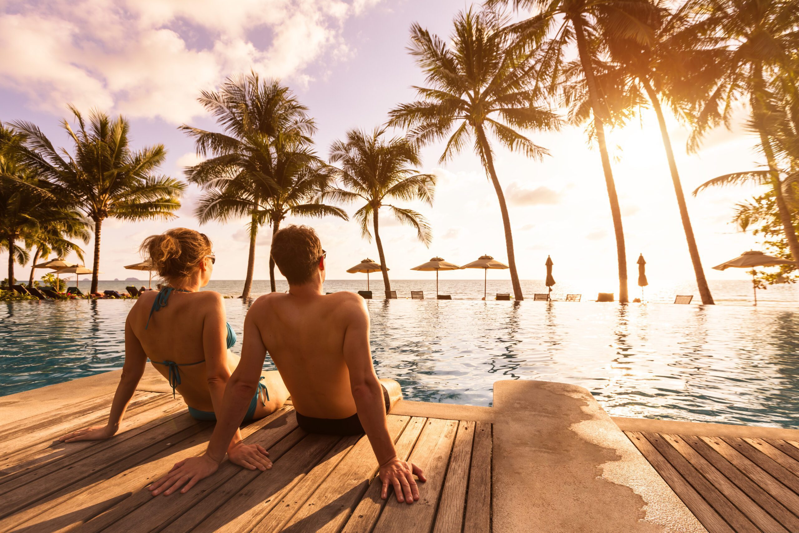 Couple enjoying beach vacation holidays at tropical resort with swimming pool and coconut palm trees near the coast with beautiful landscape at sunset, honeymoon destination